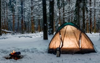Winter forest with tent and small campfire.