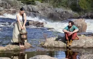 Man and woman in a river with a water pail.
